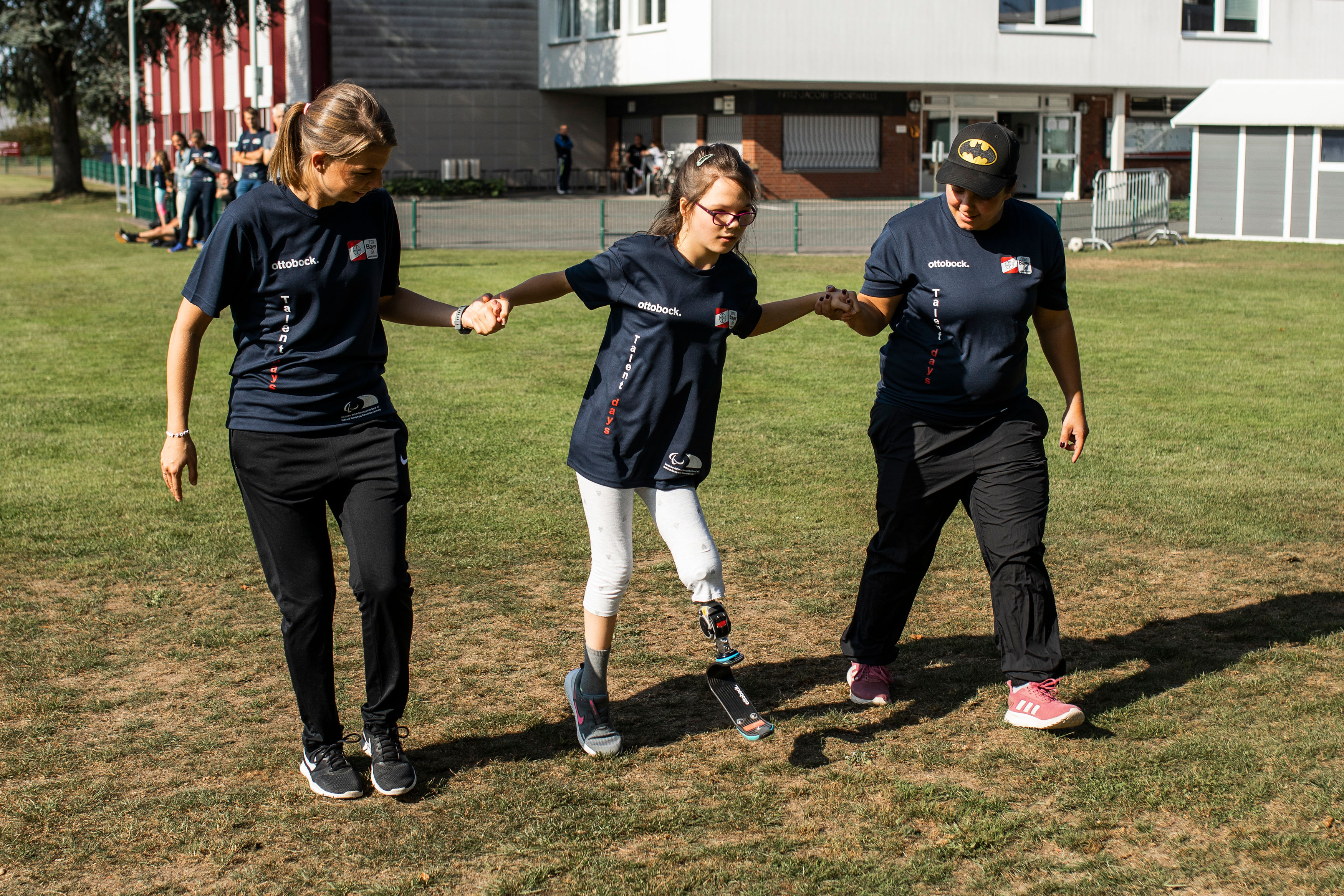 Ein Mädchen lernt das Laufen mit einer Sportprothese und wird von zwei Ehrenamtlichen begleitet | Foto: © Mika Volkmann