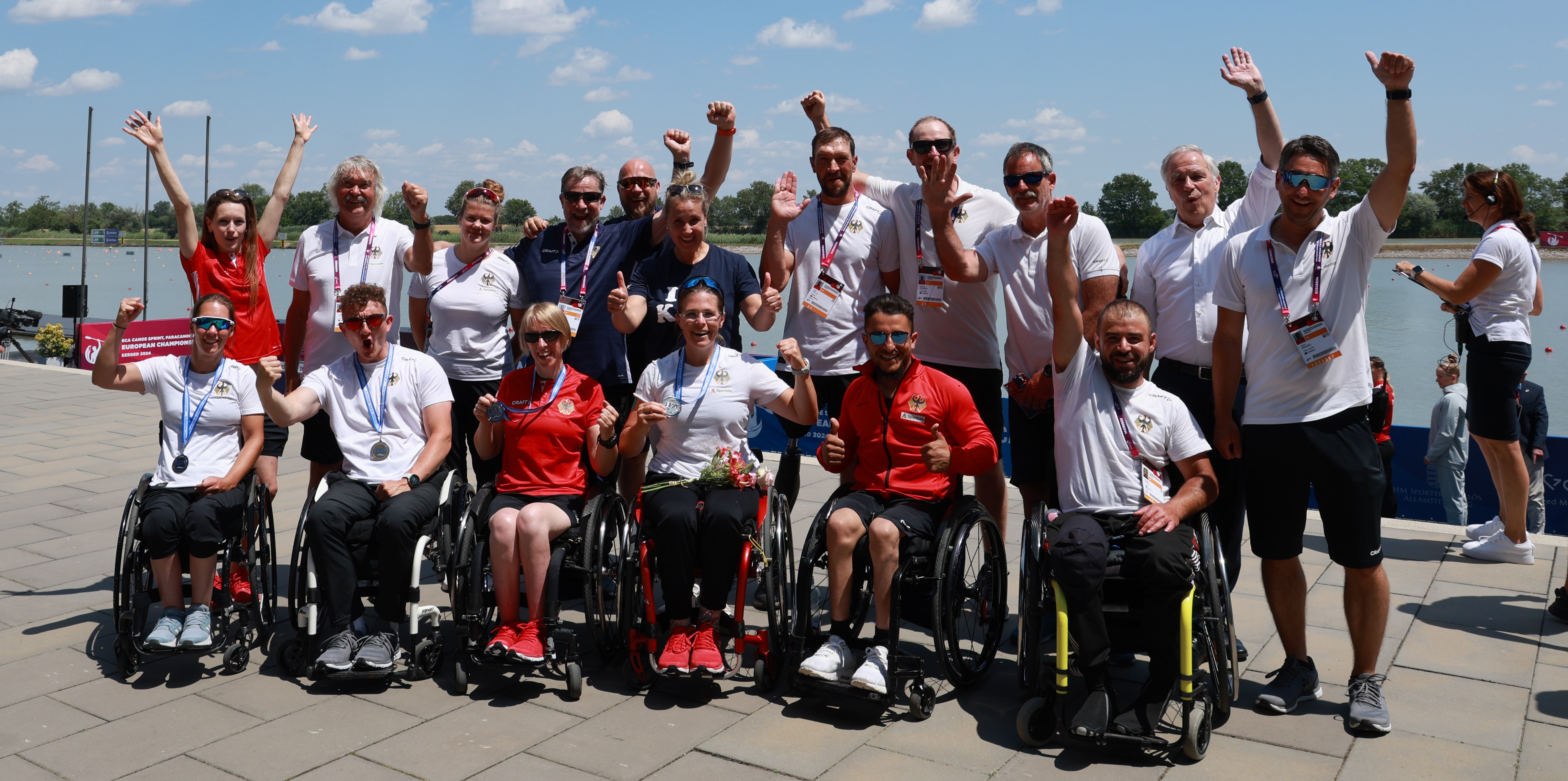 Gruppenbild des ganzen Teams (Rollstuhlfahrende vorn, stehende hinten) mit fröhlichen Gesichtern bei Sonne am Pier.